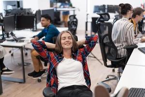 Casual business woman taking a break with legs on her table while working on desktop computer in modern open plan startup office interior. Selective focus photo