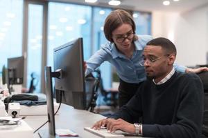 Young smiling woman explaining to serious African American coworker project strategy. Diverse startup coworkers students woman and man talking discussing working in modern office using computer. photo