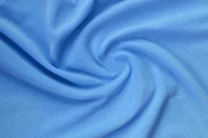 The blanket of furry blue fleece fabric. A background of light blue soft plush fleece material with a lot of relief folds photo