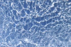 Defocus blurred transparent blue colored clear calm water surface texture with splash, bubble. Shining blue water ripple background. Surface of water in swimming pool. Blue bubble water shining. photo