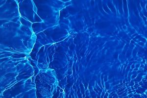 Defocus blurred transparent blue colored clear calm water surface texture with splash, bubble. Shining blue water ripple background. Surface of water in swimming pool. Blue bubble water shining. photo