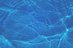 desenfoque borroso transparente color azul claro agua tranquila textura superficial con salpicaduras, burbujas. fondo de ondulación de agua azul brillante. superficie del agua en la piscina. agua de burbujas azul brillante. foto