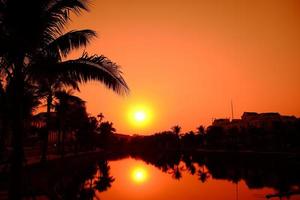 Defocus blurred dark palm trees silhouettes on colorful tropical lake sunset background, a cityscape with an orange sunset. photo