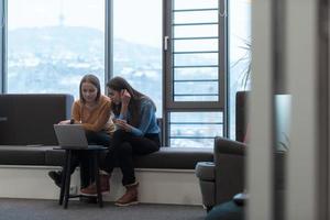 Two business women sitingt in a modern coworking space on a break from work and relax using a laptop. Selective focus photo