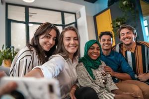 Group of business people during break from the work taking selfie picture while enjoying free time in relaxation area at modern open plan startup office. Selective focus photo