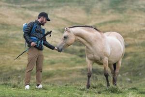 Man during a hike hands grass to a horse photo