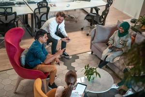 Multiethnic startup business team having brainstorming in relaxation area of modern office interior working on laptop and tablet computer photo