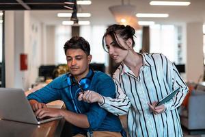Multiethnic business people man with a female colleague working together on tablet and laptop computer in relaxation area of modern startup office photo