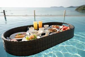 Breakfast set in tray in swimming pool, floating breakfast in tropical resort villa with ocean view. photo
