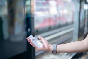 mujer con mascarilla y desinfectante de gel de alcohol para desinfectar el virus covid-19 en la estación de metro. foto