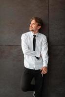 retrato de un nuevo hombre de negocios con una camisa blanca y una corbata negra parado frente a una pared gris afuera foto