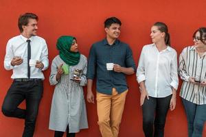 Multiethnic group of casual businesspeople using smartphone during a coffee break from work in front of the red wall outside. photo