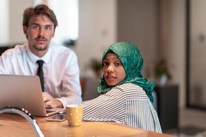 International multicultural business team.Man and muslim woman with hijab working together using smartphone and laptop coxation area at modern open plan startup officemputer in rela photo