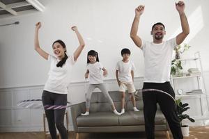 feliz bienestar familia tailandesa asiática, padres e hijos son divertidos jugando hula hoops juntos, entrenamiento físico y ejercicio saludable en la sala de estar blanca, el estilo de vida doméstico y la actividad de fin de semana. foto