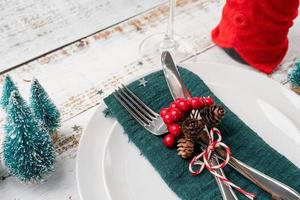 Christmas table setting with white dishware, silverware and red and green decorations on white wooden background. High angle view. photo