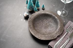 Christmas table setting with black dishware, silverware and green decorations on dark background. Top view. photo