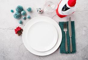 Christmas table setting with white dishware, silverware and red and green decorations on white wooden background. Top view. photo