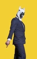 A vertical shot of a creative man in a costume with a white horse mask posing on a yellow background wall. photo