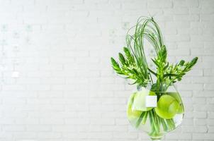 un primer plano de la planta de ornithogalum y las manzanas en un vaso grande de vidrio sobre una mesa foto