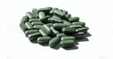 Pills of chlorella, spirulina, barley grass on white background with dark shadows close-up Nutritional supplement, detox superfood photo