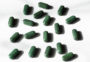 Pills of chlorella, spirulina, barley grass on white background with dark shadows close-up Nutritional supplement, detox superfood photo