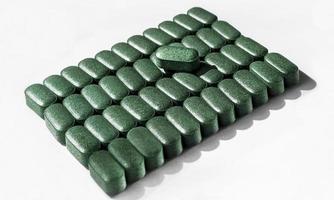 Pills of chlorella, spirulina, barley grass close-up lined up in rows on white background Nutritional supplement, detox superfood health care photo