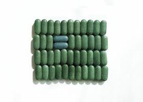 Chlorella, spirulina or barley grass in pill shaped rows and two blue pills across on white background Nutritional supplement, detox superfood health care photo