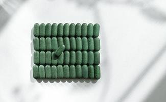 Pills of chlorella, spirulina, barley grass close-up lined up in rows on white background with shadow pattern Nutritional supplement, detox superfood health care photo