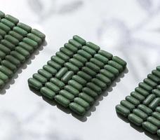 pattern of pills of chlorella, spirulina, barley grass close-up lined up in rows on white background with shadow pattern Nutritional supplement, detox superfood health care photo