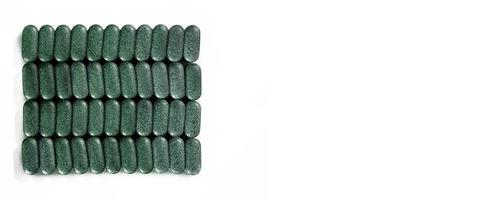 Pills of chlorella, spirulina, barley grass close-up in rows on white background Nutritional supplement, detox superfood health care banner copy space photo