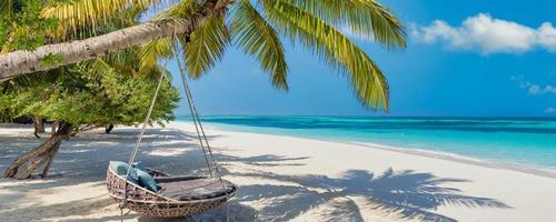 Beautiful Maldives. Tropical beach panorama as summer landscape, beach swing or hammock, sea sand sky for luxury beach banner. Perfect beach coast vacation and summer holiday. Tranquil paradise island photo