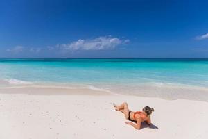 Young sexy woman relax on the beach. Perfect tropical island, beach shore, with turquoise ocean lagoon. Bikini, long legs, sunglasses enjoying summer vacation. Carefree woman beach portrait, leisure photo