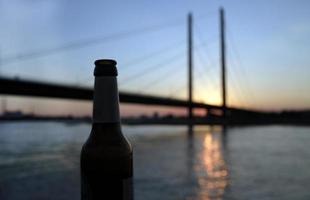 botella de cerveza y una puesta de sol en el río rin en dusseldorf, alemania foto
