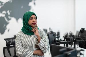 Portrait of muslim black female software developer with green hijab standing at modern open plan startup office. Selective focus photo