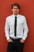 retrato de un nuevo hombre de negocios con una camisa blanca y una corbata negra parado frente a una pared roja afuera foto