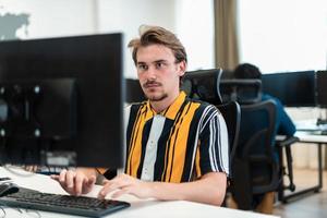 Casual man working on desktop computer in modern open plan startup office interior. Selective focus photo
