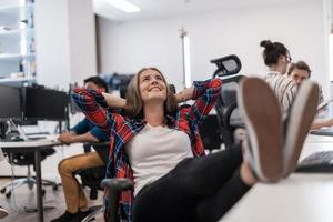 Casual business woman taking a break with legs on her table while working on desktop computer in modern open plan startup office interior. Selective focus photo