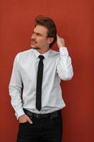 Portrait of startup businessman in a white shirt with a black tie standing in front of red wall outside photo