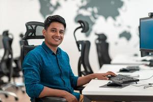 Casual business man working on desktop computer in modern open plan startup office interior. Selective focus photo