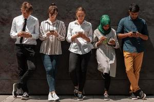 grupo multiétnico de empresarios casuales que usan teléfonos móviles durante la pausa para el café del trabajo frente a la pared negra afuera foto