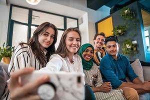 Group of business people during break from the work taking selfie picture while enjoying free time in relaxation area at modern open plan startup office. Selective focus photo