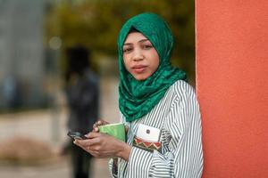 African Muslim businesswoman with green hijab using mobile phone during coffee break from work outside photo