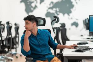 Casual business man working on desktop computer in modern open plan startup office interior. Selective focus photo