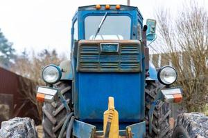 vieja foto frontal del tractor azul con valla y árboles en el fondo