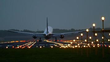 The wide bodied aircraft lands on the illuminated runway in the early morning video