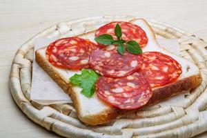 Salami sandwich on wooden board and wooden background photo