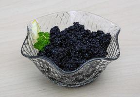 caviar negro en un recipiente sobre fondo de madera foto