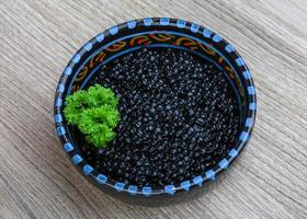 caviar negro en un recipiente sobre fondo de madera foto