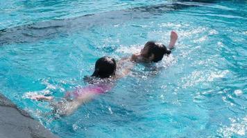 irmãzinhas felizes brincam na piscina ao ar livre do resort tropical durante as férias de verão em família. crianças aprendendo a nadar. atividades de verão saudáveis para crianças. video
