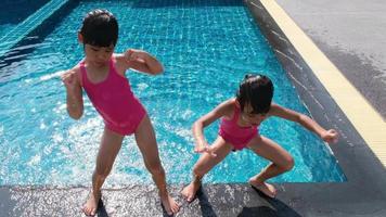 gelukkige zusjes spelen in het buitenzwembad van tropische resort tijdens familie zomervakantie. kinderen leren zwemmen. gezonde zomeractiviteiten voor kinderen. video